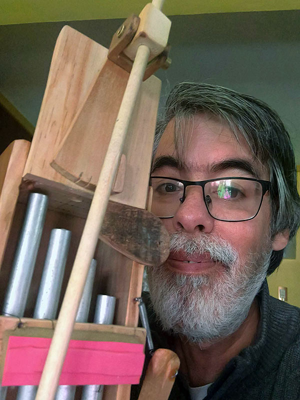 Sebastán Musso sosteniendo un instrumento musical informal de madera clara y cuatro tubos de metal brillante.